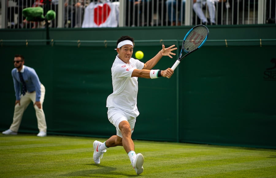 Kei Nishikori of Japan plays a backhand at Wimbledon 2019